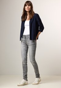 Camisa de botones de color marino sobre una camiseta blanca, combinada con jeans ajustados grises y zapatillas blancas con acentos verdes. Tela suave, estilo ajustado.