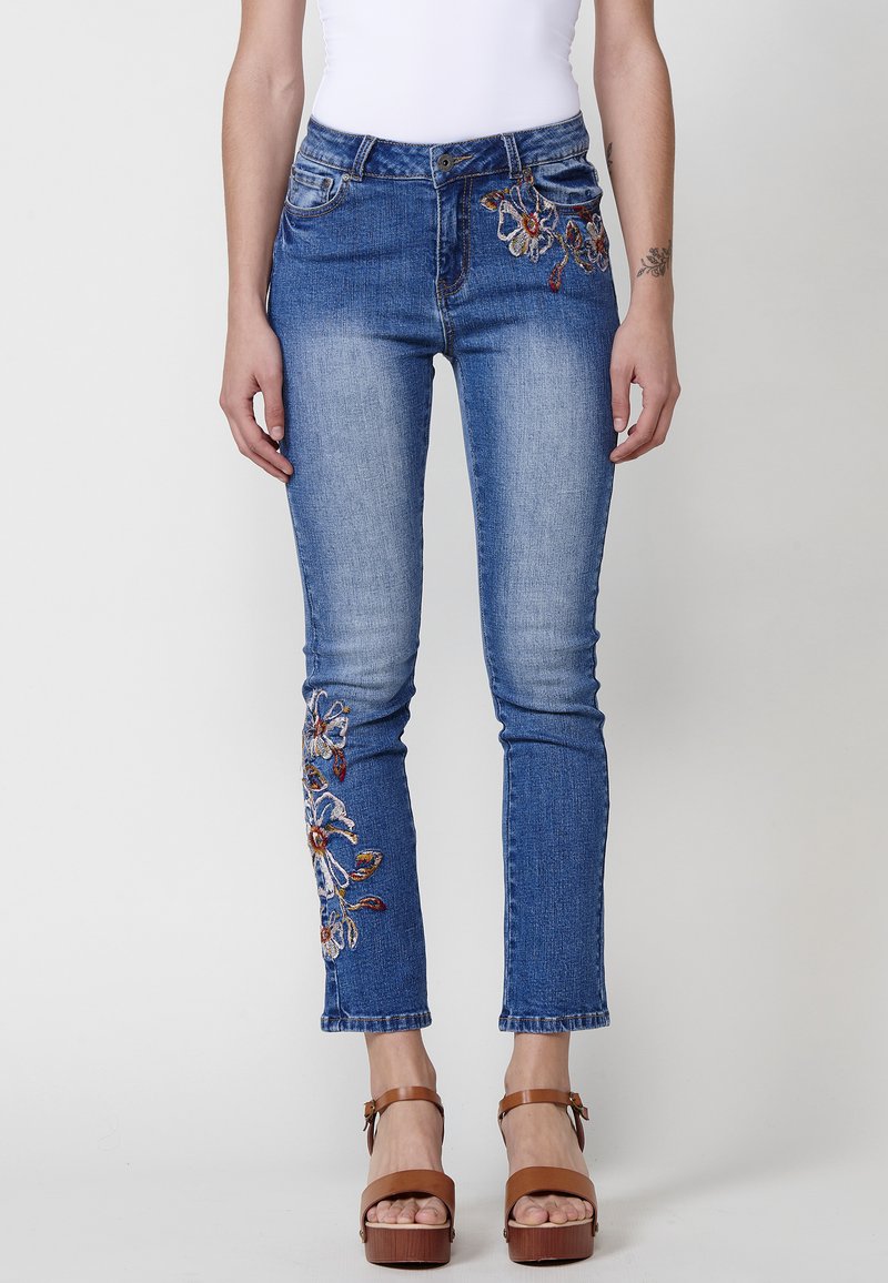 Broderade blåjeans i denim med blommönster i färger som röd och vit, med smal passform och avkortad längd, kompletterat med en knappmidja.