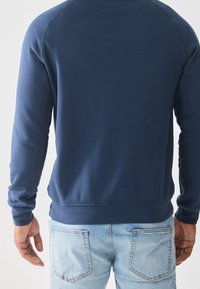 Sudadera azul marino con mangas largas, puños y dobladillo acanalados; tela de textura suave; combinada con vaqueros azul claro.