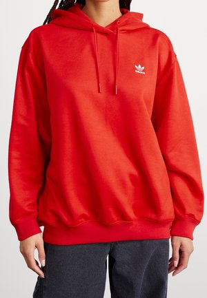 Haut à capuche rouge en tissu doux, doté d'une poche kangourou, d'une capuche à cordon réglable et du logo Adidas blanc sur la poitrine.