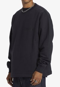 Sudadera de un oscuro color navy con cuello redondo, con un logo texturizado en el pecho, puños acanalados y un ajuste relajado.