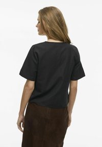 Svart kortärmad topp i en avslappnad passform, med rundad halsringning. Tyget är mjukt och kombineras med en kjol i brunt mocka.