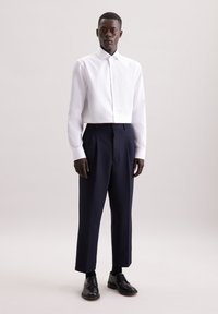 Witte overhemd met knopen, marineblauwe geplooide broek en zwarte schoenen; slim fit met een gladde textuur en strakke lijnen. Geen patronen of accenten.