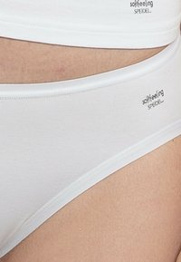 Weiße Baumwollunterhose mit glatter Textur, verfügt über einen tiefen Schnitt und einen weichen, elastischen Bund. Markenlogo "softfeeling" aufgedruckt.