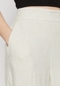 Pantalones de lino en un color beige claro con un acabado texturizado. Presenta un corte relajado y bolsillos laterales. Diseño simple y limpio.