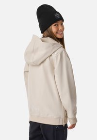 Felpa beige con zip e cappuccio ampio, polsini a costine e tasche laterali. Berretto nero con etichetta logo sul davanti. Texture liscia.