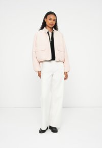 Veste bomber rose clair raccourcie avec deux poches avant, dotée d'un col rond et de poignets élastiques, associée à un pantalon large blanc.