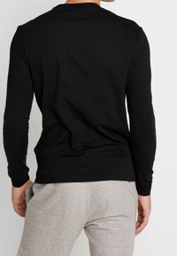 Schwarzes Langarmshirt mit rundem Ausschnitt, glatter Textur, figurbetontem Design, kombiniert mit hellgrauen Jogginghosen mit elastischem Bund.