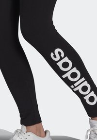 Svarta leggings med tajt passform, prydda med en framträdande vit "adidas"-logotyp längs sidan. Tillverkade av stretchigt material, utformade för komfort.