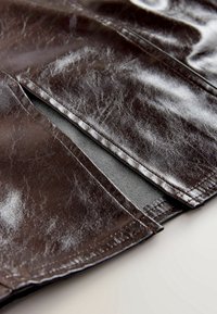 Gros plan d'un tissu en cuir marron foncé montrant une fente de ventilation avec des coutures visibles et une surface texturée.