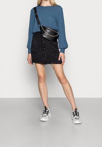 Niebieska bluzka z długim rękawem w wzory o luźnym kroju, w połączeniu z czarną mini spódnicą z kordurowej tkaniny z przednimi guzikami oraz białymi butami sportowymi.