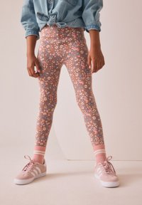 Blomstrede leggings i pastelrosa og blå, lavet af elastisk materiale. Kombineret med rosa sneakers med hvide striber og rosa sokker.