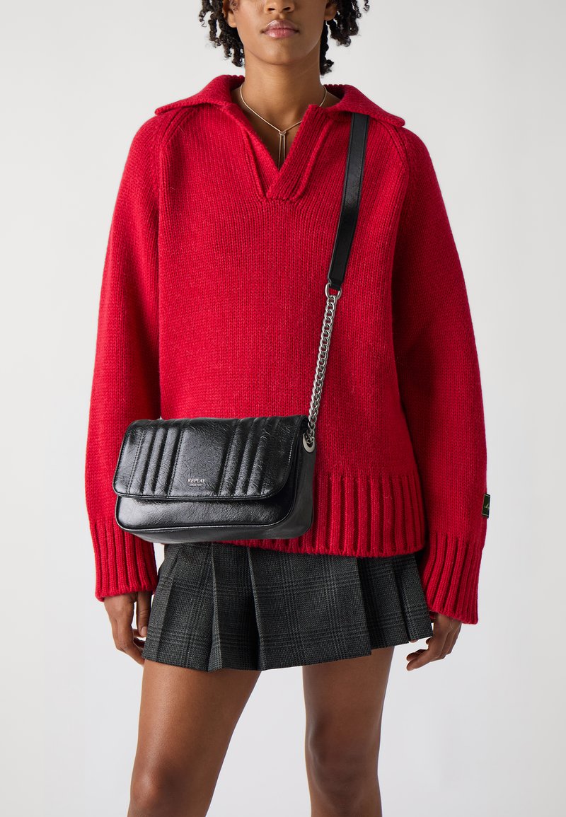 Suéter rojo de punto con cuello tipo camisa, combinado con un bolso bandolera negro acolchado y una falda texturizada plisada con estampado de cuadros.