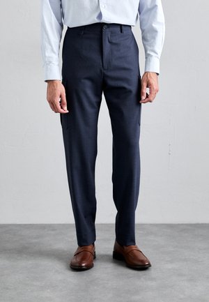 Navy blue tailored trousers with side pockets, crafted from smooth wool blend fabric. Paired with brown leather shoes.