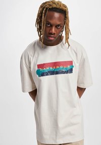 Beige oversized tričko vyrobené z bavlny má na přední straně barevný grafický design s výrazným žlutým nápisem "DANGEROUS".
