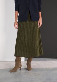 Green ribbed knit skirt with a long, flowing design, paired with brown suede boots featuring a pointed toe and a zip closure.