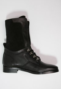 Botines negros con una combinación de cuero y ante, con cordones en la parte delantera y herrajes metálicos, y un tacón bajo y sólido.