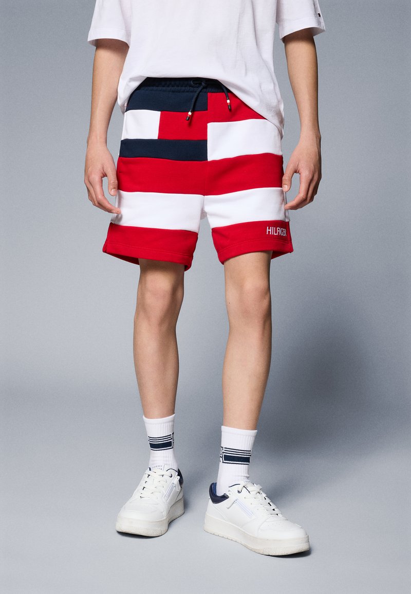 Röd och vit randig shorts med en marinblå midja, med snörning och "HILFIGER" broderi på nedre benet. Åt tillsammans med vita sneakers.