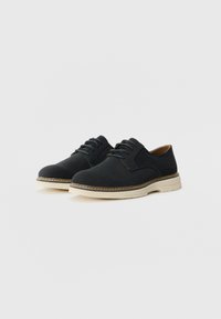 Schwarze Wildleder-Schnürschuhe mit runder Zehenpartie, beiger Gummisohle und kontrastierender Naht entlang der Kante. Glatte Textur, minimalistisches Design.