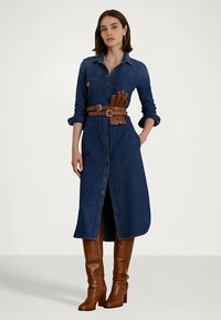 Moteris vilkinti ilgą džinsinį suknelę su sukrautomis rankovėmis, rudos odinės diržo su pirštinėmis, ir atitinkamais rudos odos aukštakulniais auliniais batais iki kelių.