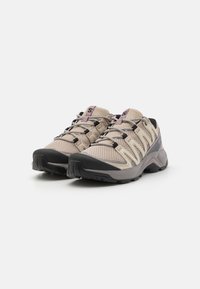 Chaussures de randonnée en mesh respirant couleur beige clair avec des accents violets, lacets élastiques et semelle extérieure en caoutchouc noir pour une meilleure traction. Design profil bas, durables.