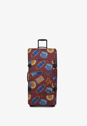 Valise à roulettes rouge et bleue à motifs, avec des patchs, des sangles ajustables, une poignée extensible et des roues en caoutchouc. Le matériau semble durable et texturé.