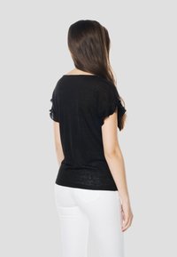 Must lühikeste varrukatega pluus, mille lõige on lahtine. Omaduseks on volangidega varrukad ja lai kaelus. Valmistatud kergekaalus kangast. Sobitatud valgete pükstega.