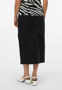 Falda midi de mezclilla negra con un corte recto, detalles en las costuras laterales, combinada con zapatos de tacón blancos y una blusa con estampado.