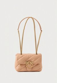 Τσαντάκι σε μπεζ δέρμα με καπιτονέ σχέδιο και χρυσή αλυσίδα, διακοσμημένο με δαχτυλίδι και λεπτομέρεια πουλιού στο μπροστινό μέρος. Συμπαγές ορθογώνιο σχήμα.