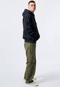 Navy hooded sweatshirt with a drawstring, paired with olive cargo pants featuring multiple pockets. Model wears beige sneakers.