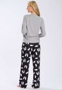 Top gris de manga larga combinado con pantalones de pijama negros que presentan un patrón repetido de conejitos blancos. Tejido suave con un corte holgado.