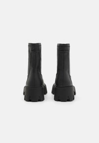 Bottes noires en cuir avec un semelle en caoutchouc épaisse, présentant des coutures verticales et une texture lisse sur la partie supérieure.
