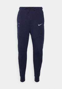 Navy fleece joggers with black drawstring, featuring a purple Spurs logo and a white Nike swoosh. Tapered leg design with ribbed cuffs.