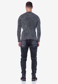 Grauer, gerippter Pullover mit langen Ärmeln, kombiniert mit schwarzen Jeans, die dekorative Nähte und eine schlanke Passform aufweisen. Beide Kleidungsstücke haben eine strukturierte Oberfläche.