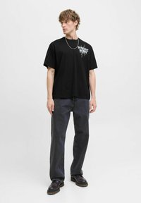 Black cotton t-shirt with short sleeves and a graphic design on the left chest, paired with dark, straight-leg jeans and black shoes.