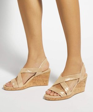 Pieds portant des sandales compensées beiges avec des sangles croisées et des talons en liège sur fond blanc.