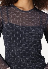 Zwarte mesh top met een stippenpatroon en bloemmotieven, lange mouwen en een ronde halslijn. Lichtgewicht en semi-doorschijnende textuur.