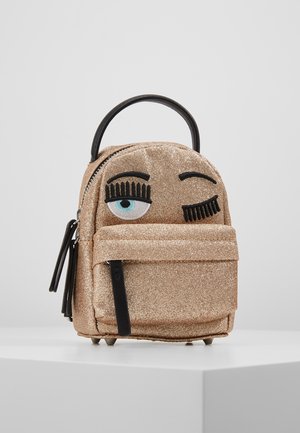 Mała, błyszcząca złota torebka z jednym haftowanym otwartym okiem i jednym mrugającym okiem, czarnym uchwytem i przednią kieszenią na zamek, na białej powierzchni.