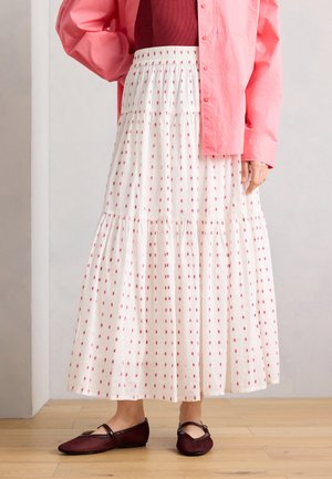 White tiered maxi skirt with small red floral pattern worn with pink shirt and maroon top, paired with dark red woven Mary Jane flats.