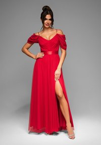 Robe de soirée rouge avec manches dénudées, corsage ajusté, jupe fluide avec une fente haute sur la cuisse et une ceinture en satin.