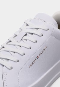 Λευκό αθλητικό παπούτσι Tommy Hilfiger με λευκά κορδόνια, δέρμα με λείο υφή και λογότυπο τυπωμένο σε χρυσό και κόκκινο στη πλευρά.