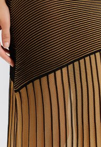 Čierna a zlatá priehľadná tkanina s vertikálnymi pruhmi; spodná časť má tenké pruhy. Hladká textúra, vodorovné pásy v hornej časti.