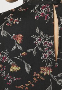 Robe noire à fleurs avec des fleurs rouges, jaunes et grises vibrantes, des motifs de feuilles complexes, un tissu texturé et un détail dos en forme de trou de serrure.