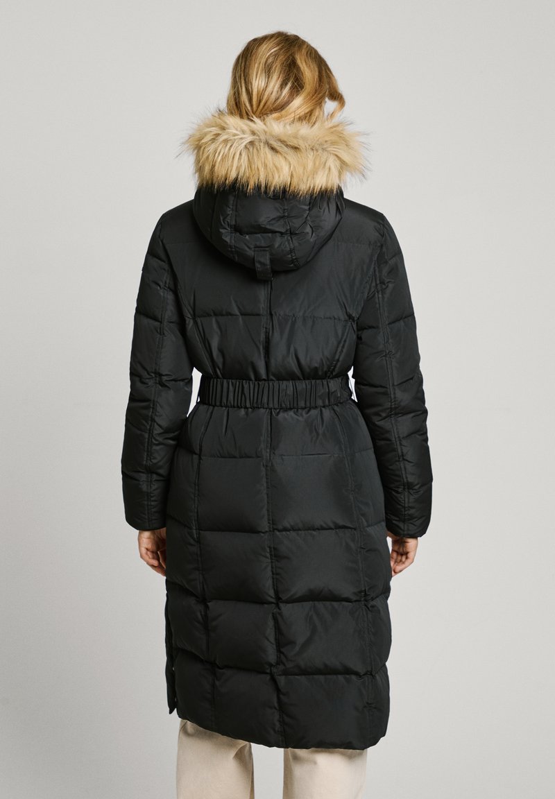Giacca piumino nera con cappuccio foderato in pelliccia sintetica, vita strizzata e texture trapuntata. La giacca arriva fino a metà polpaccio per una maggiore calore.