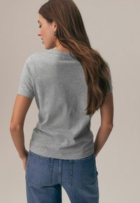 Siva majica kratkih rokavov z mehko teksturo, okroglim ovratnikom in prilegajočim se krojem, kombinirana z izzbledenimi modrimi kavbojkami z visokim pasom.