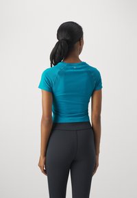 Maglietta atletica a maniche corte color teal con design aderente e retro testurizzato, abbinata a leggings neri a vita alta, che mettono in mostra una silhouette snella.