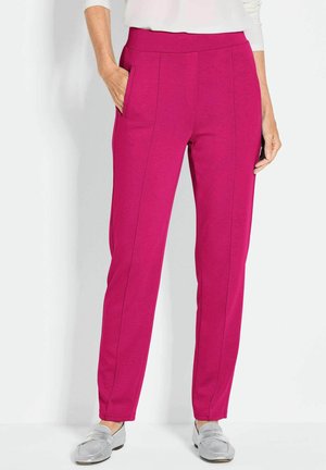 Fuchsia stretchbroeken met een platte tailleband, zijzakken en verticale naden. Gepaarde met zilveren instappers op een neutrale achtergrond.