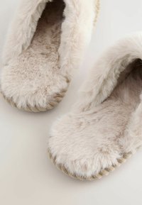 Fuzzy beige slippers with a soft, plush texture, rounded toe, and braided fabric around the soles. Indoor footwear design.