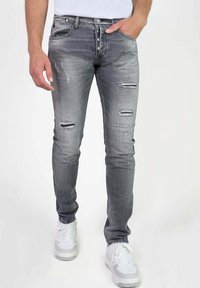 Vervaagde grijze denim jeans met gescheurde accenten, vijf-pocket ontwerp, slim fit en metalen knoopsluiting, gecombineerd met witte sneakers.