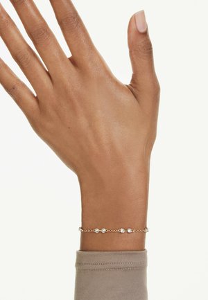 Guldtonet kædearmbånd med flere klare, ovale sten sat i et delikat design. Bæres på en neutraltonet ærme.